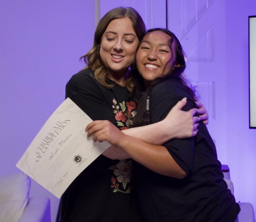 A Joyco leader hugs a smiling student holding her certificate of completion